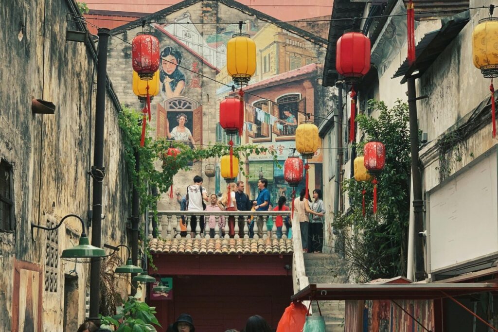 Gambar ini tunjukkan lorong dengan lampu-lampu pelita cantik, dinding berseni mural, dan orang ramai. Di Instagram Malaysia, gunakan gamba seronok seperti ini untuk promosi jenama dengan menarik minat pengguna.