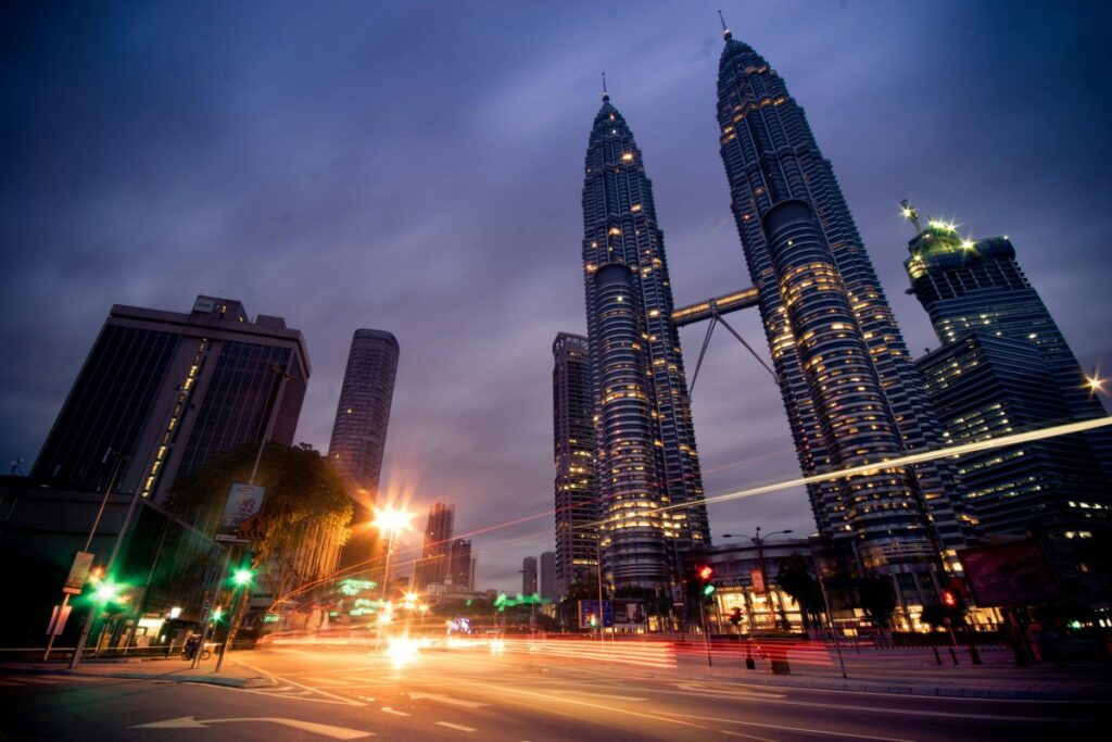 Gambar menunjukkan Menara Berkembar Petronas yang megah di Kuala Lumpur sewaktu malam. Lampu - lampu di bangunan - bangunan itu berseri - seri, manakala jalan raya penuh dengan sinar - sinar kilas balas kenderaan. Ramalan Pemasaran Media Sosial di Malaysia 2025: Bentangan kota ini dengan landmark ternama Malaysia boleh menjadi inspirasi untuk strategi pemasaran media sosial. Potensi untuk menggunakan imej like ini untuk menarik minat pengguna media sosial semakin besar menjelang 2025.